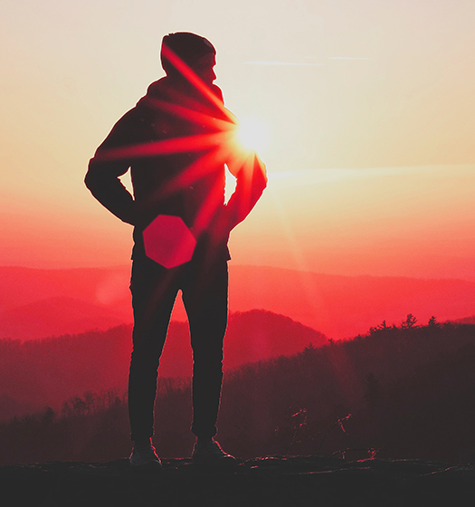 A person standing on a mountain with the sun behind them.