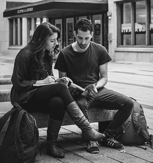 Two students sitting on a bench looking at a book.