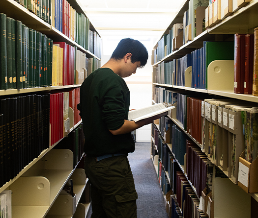 A student standing in a library looking at a book