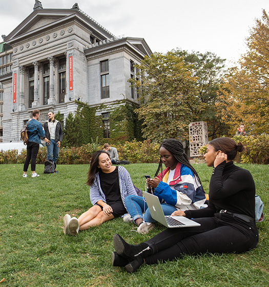 Diverse group of students socializing on the McGill's lower campus grass with Redpath museum in background