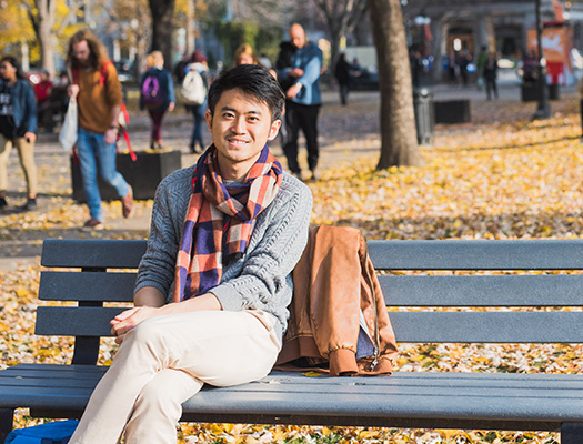 Lower campus in the autumn with student on bench with people walking on path nearby
