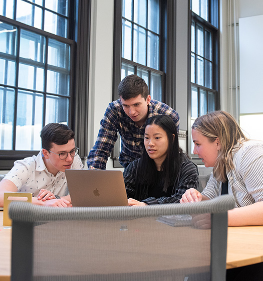 Group of four McGill students in a classroom with big windows looking at a laptop