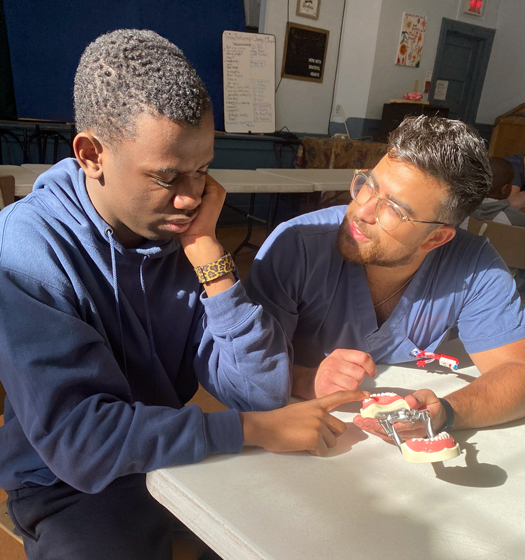 A student sitting at a table with a professor showing him a teaching model of teeth.