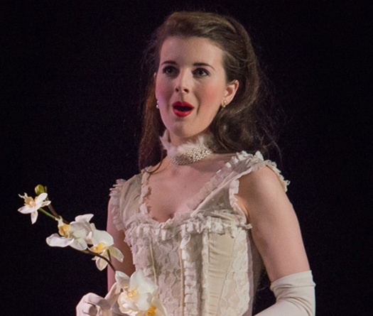 A woman in a white dress singing while holding a flower