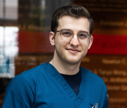 Un homme souriant, vêtu d'une blouse bleue et portant des lunettes