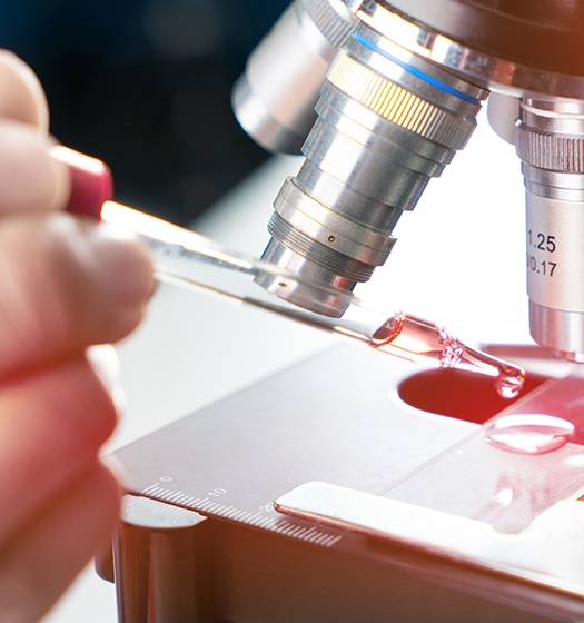 A researcher uses a dropper to view specimen on microscope slide 