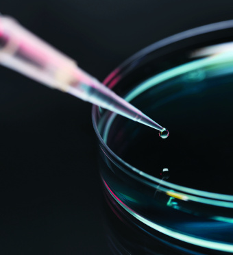 A pipette dropping a drop of liquid into a glass dish